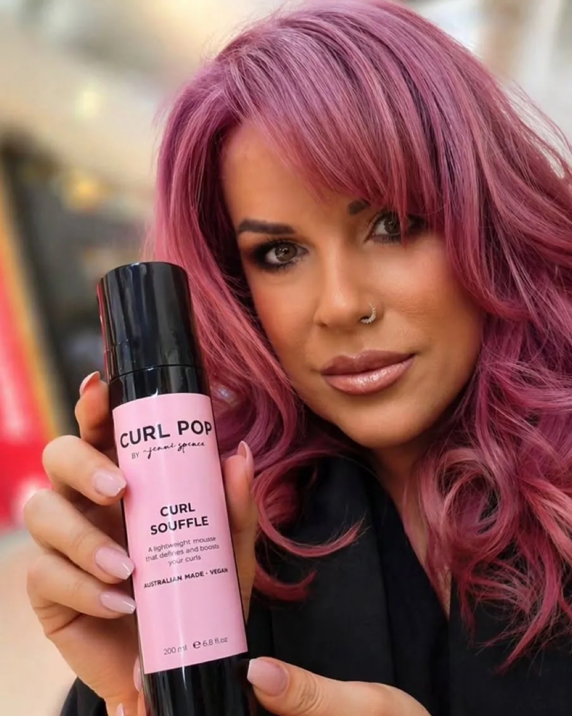 Jenni Spence, founder of Aoki Hair, with pink curls, holding her Curl Pop curl soufflé product.