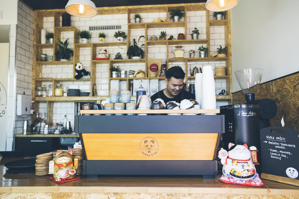 Andy Ngo behind the Panda & Co espresso bar, the brand wordmark engraved on the bamboo machine front.